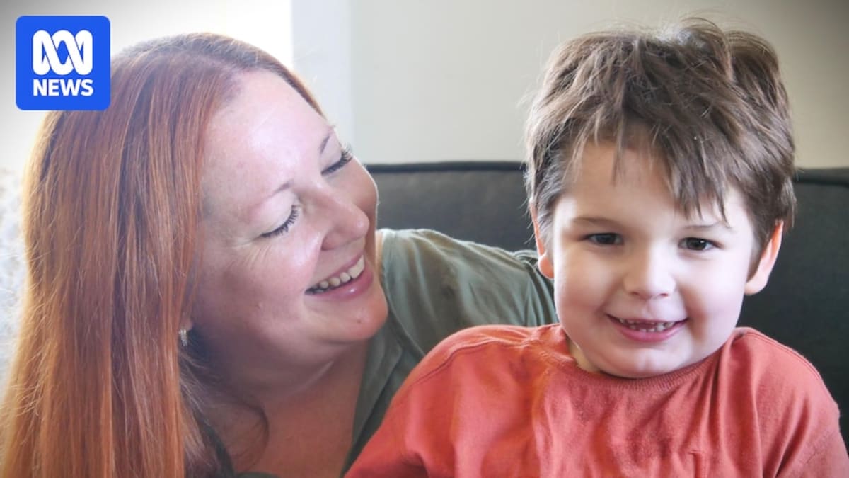 Four-year-old boy Leo smiling while sitting next to Annie, a golden-colored seizure alert dog in training