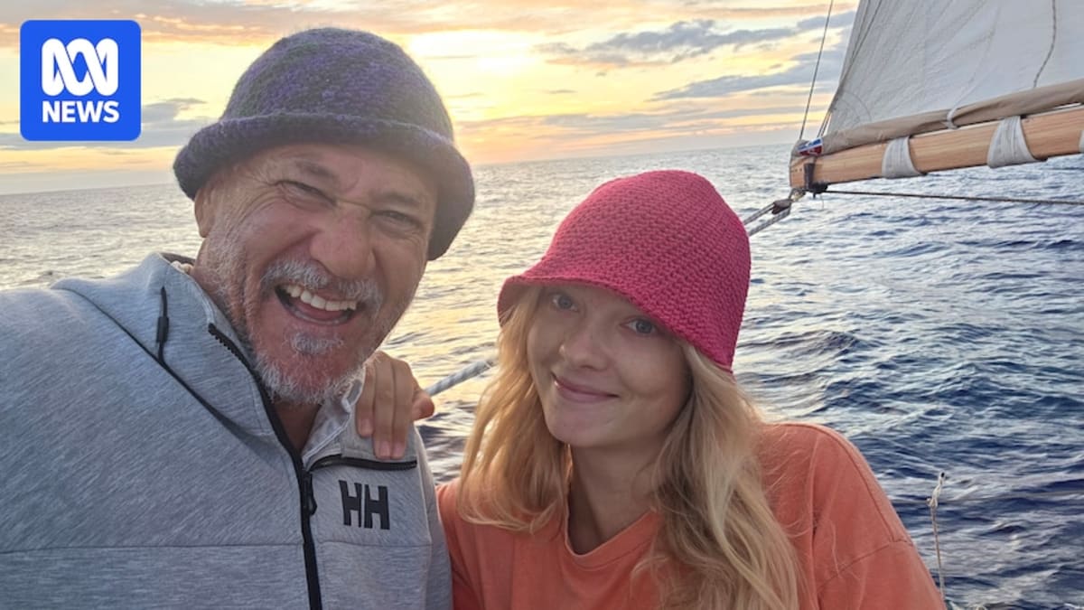 Father and daughter standing together on deck of small wooden sailing yacht at sea