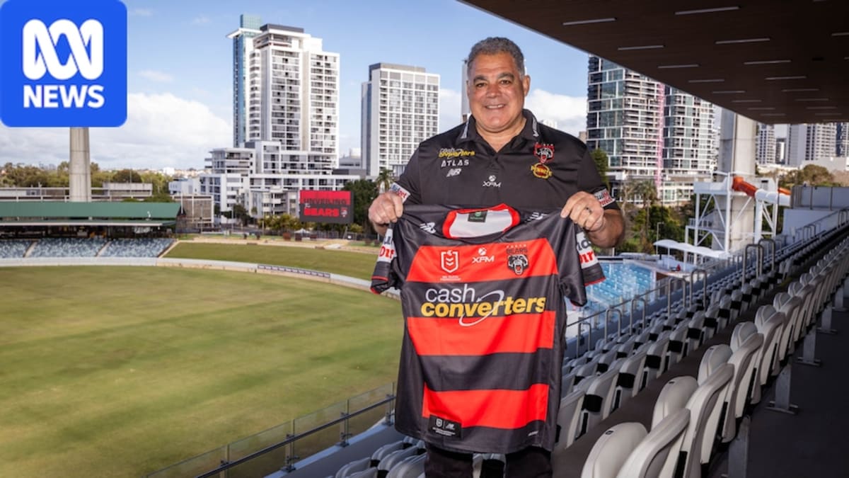 Coach Mal Meninga holding Perth Bears jersey with red hoops on black background at unveiling ceremony