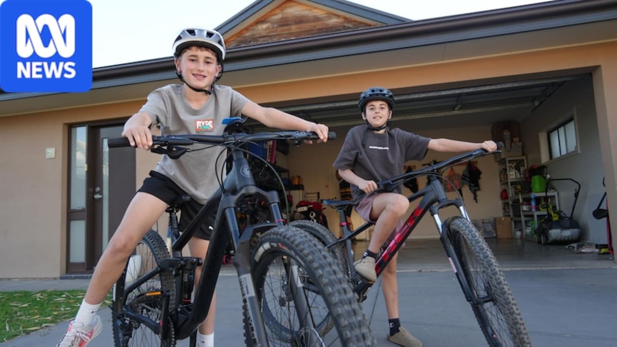 Two young boys smile while sitting on their bicycles on a residential street