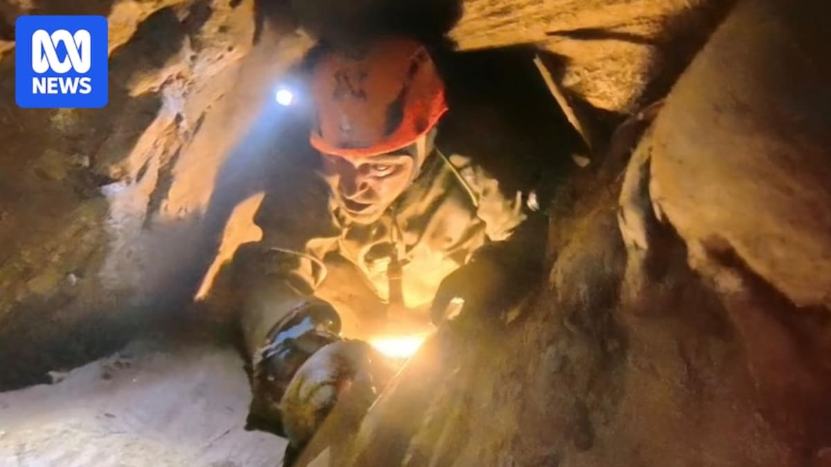 Cave diver navigating through narrow muddy passage with headlamp in flooded Laos cave system
