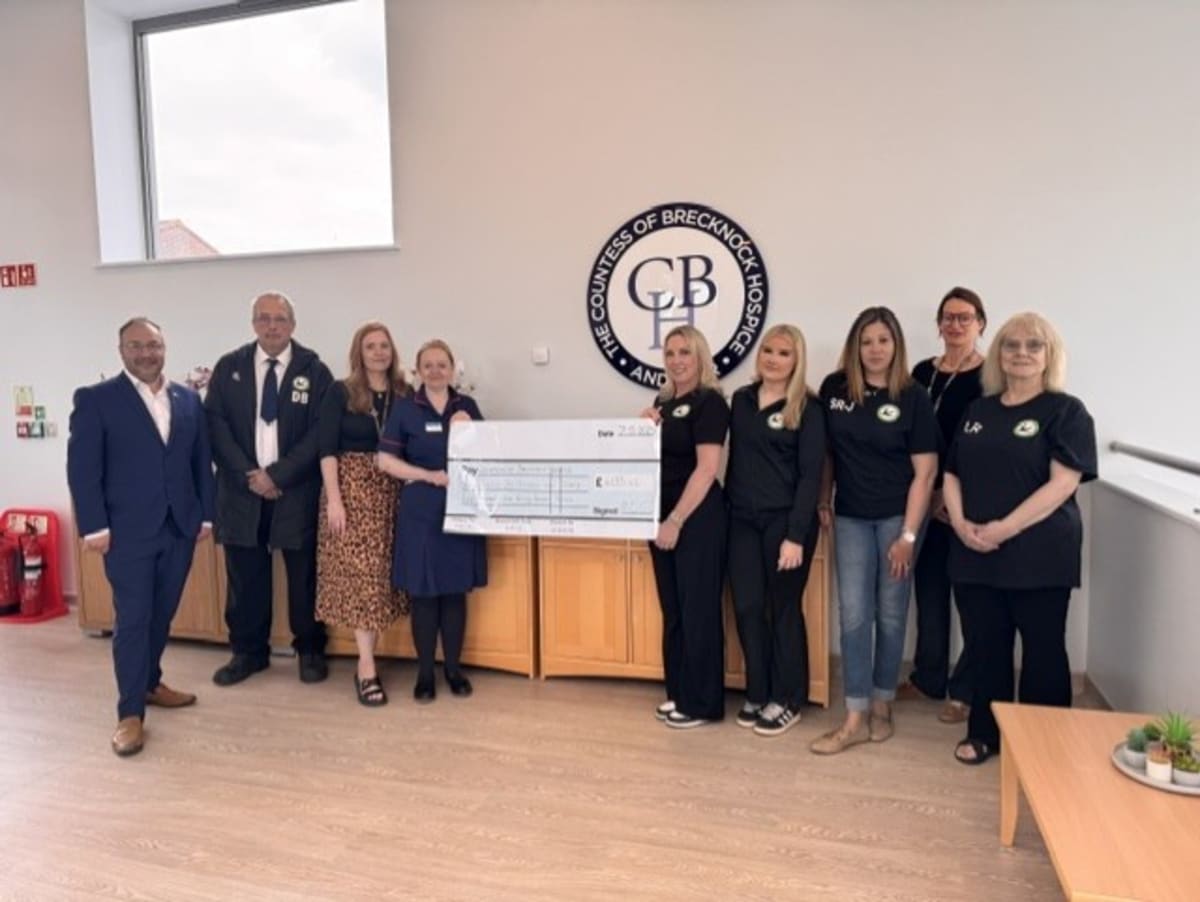Youth football players and hospice staff holding oversized charity check at stadium presentation