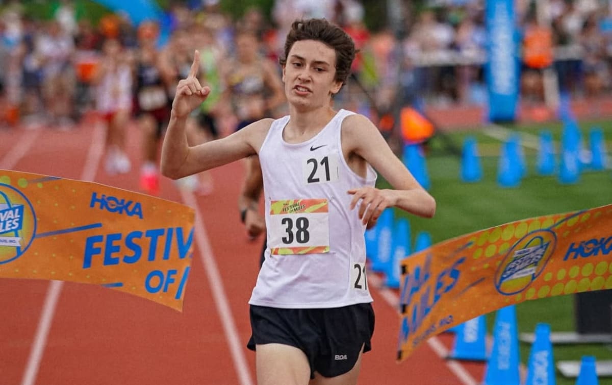 Young runner Luke Surface crossing finish line at outdoor track meet wearing white racing singlet