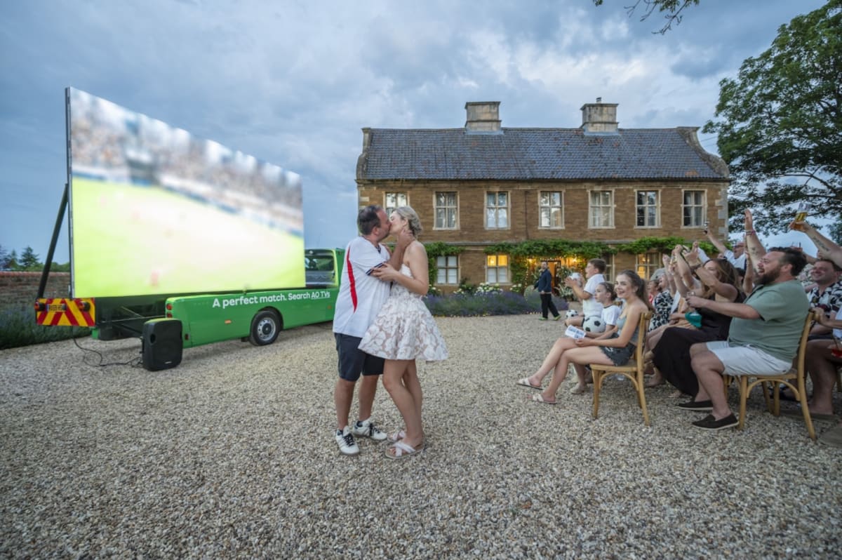 Bride and groom watching England football match on giant screen at outdoor wedding reception