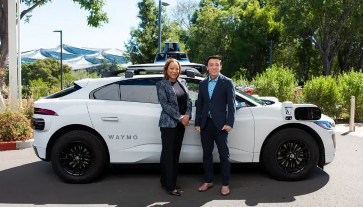 White electric Waymo self-driving vehicle navigating modern Singapore street with pedestrians and cyclists
