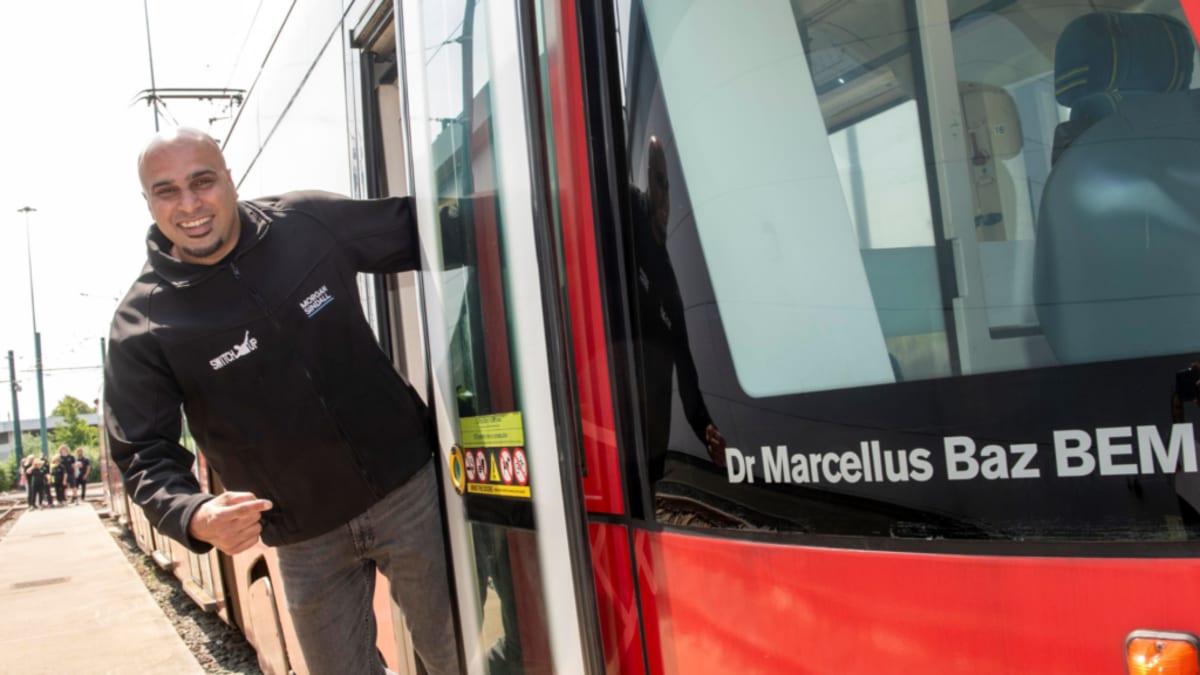 Nottingham tram traveling through city streets with community hero name displayed on side