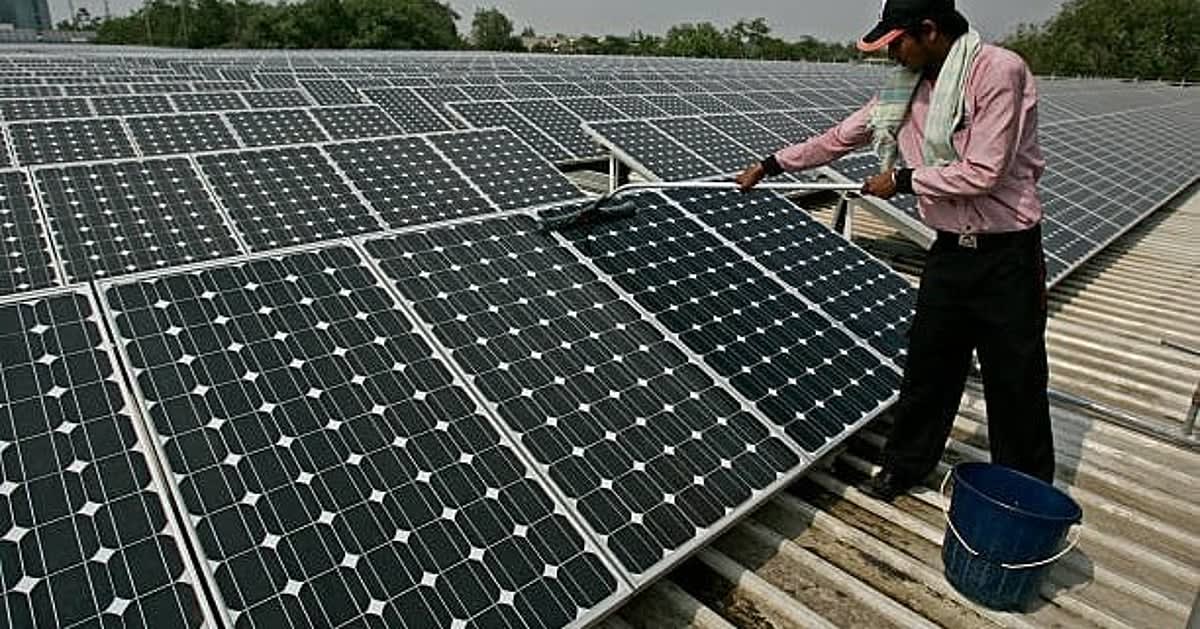 ** Solar panel arrays stretching across Indian landscape under bright blue sky with sun