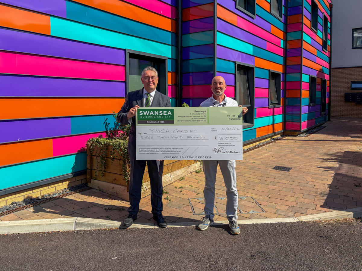Building society executive presenting oversized check to charity leader in Cardiff office