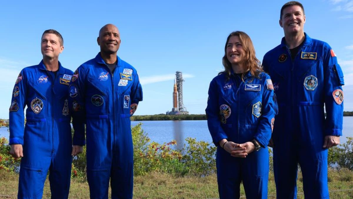 Four Artemis II astronauts in orange flight suits walking together at Kennedy Space Center
