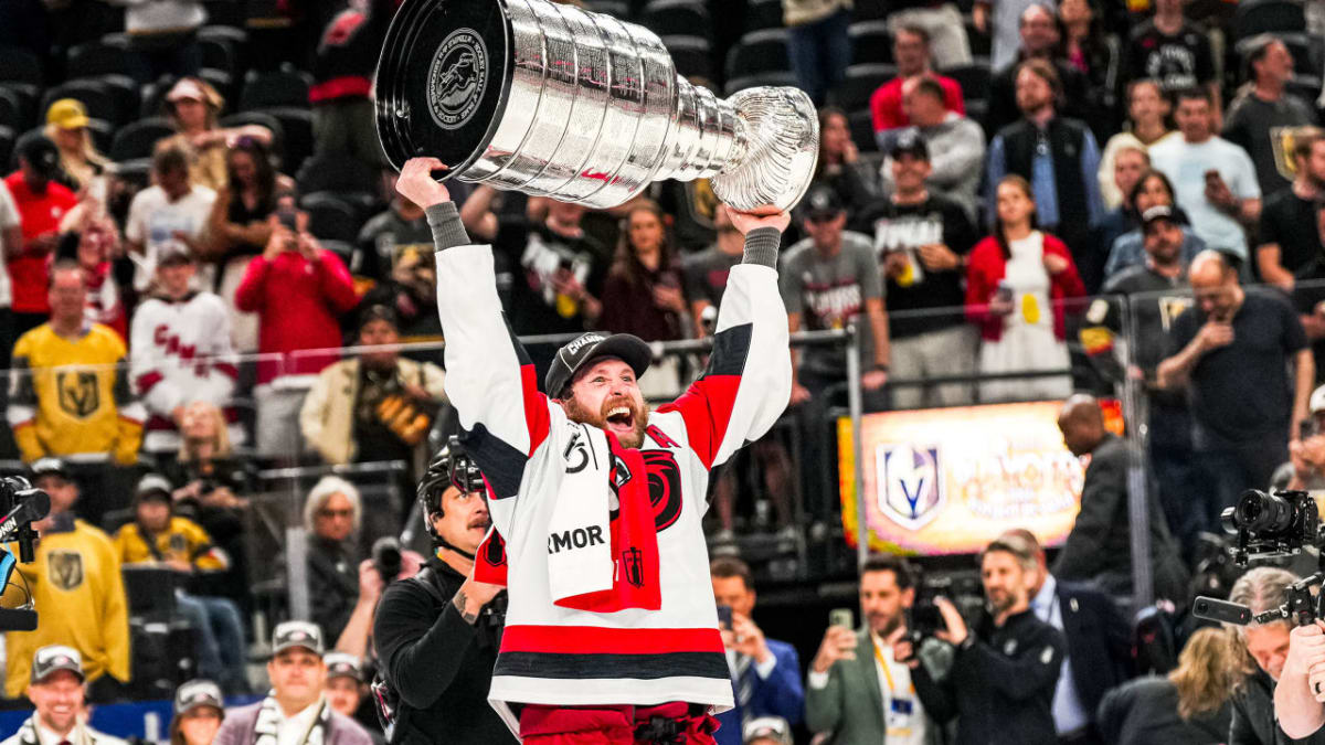 Jaccob Slavin holding Stanley Cup trophy above head surrounded by Carolina Hurricanes teammates celebrating