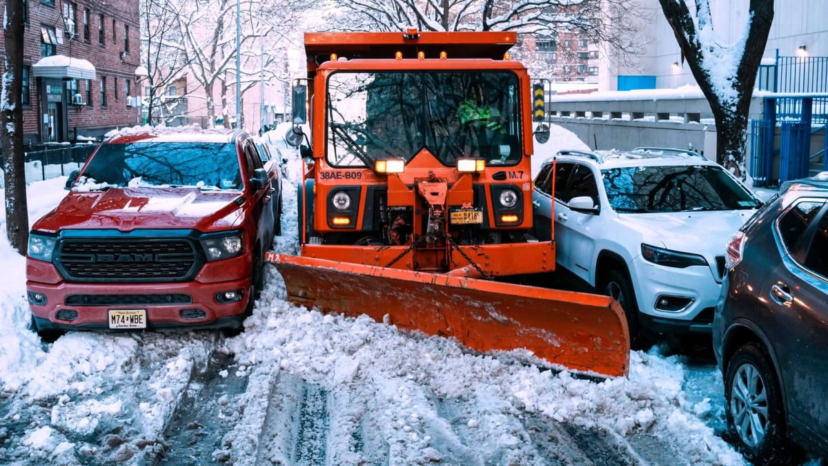 GPS-equipped snowplow clearing snowy city street with orange lights flashing during winter storm