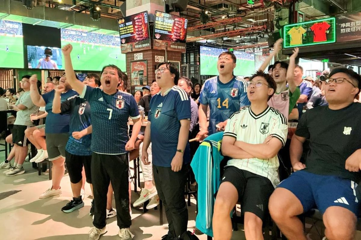 Chinese soccer fans in blue jerseys celebrating enthusiastically inside a Shanghai sports bar