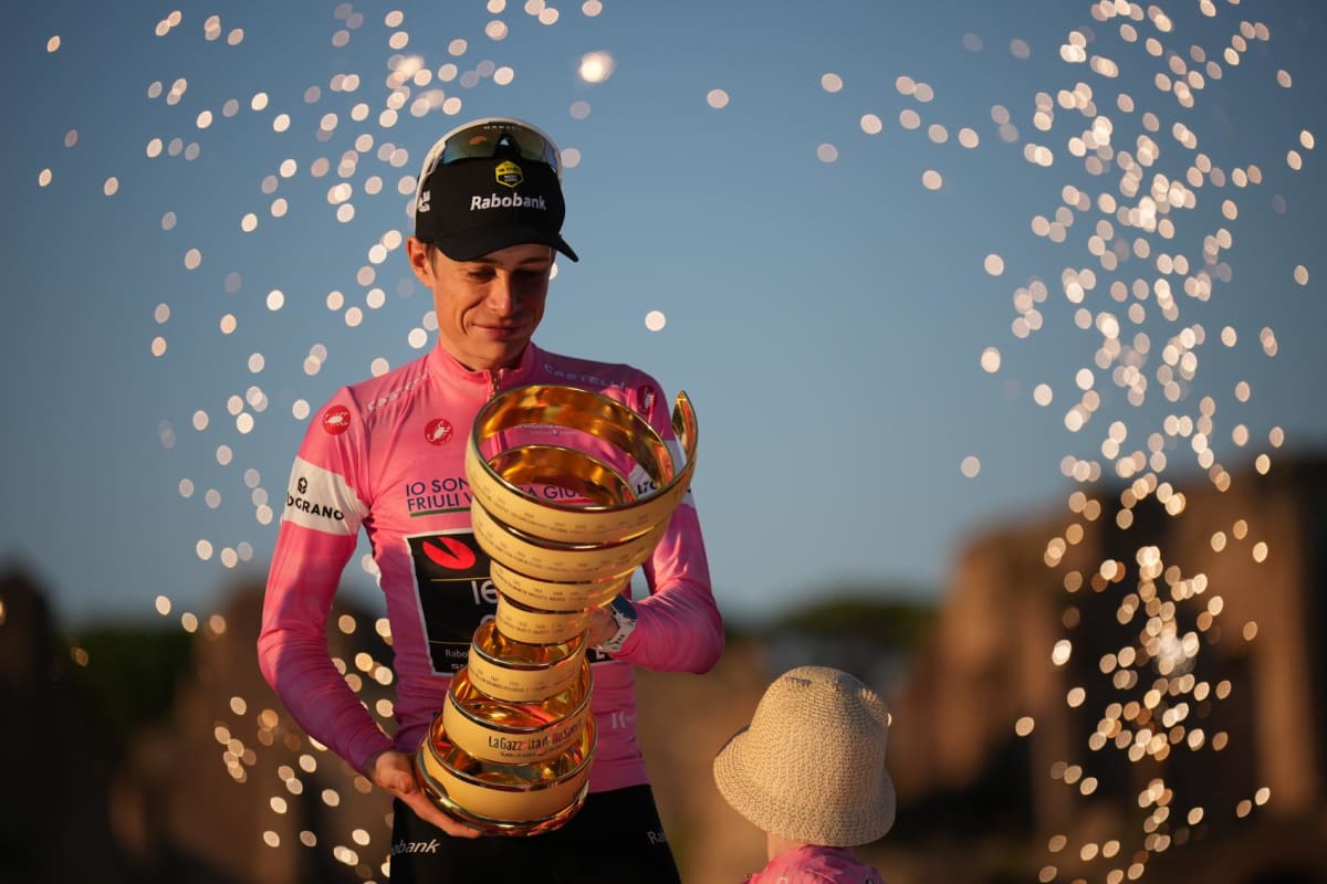 Jonas Vingegaard holding trophy on podium wearing pink jersey with his wife and two children