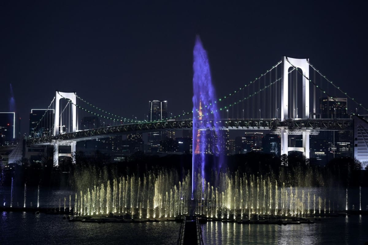 Massive illuminated fountain shooting water high into night sky over Tokyo Bay waterfront