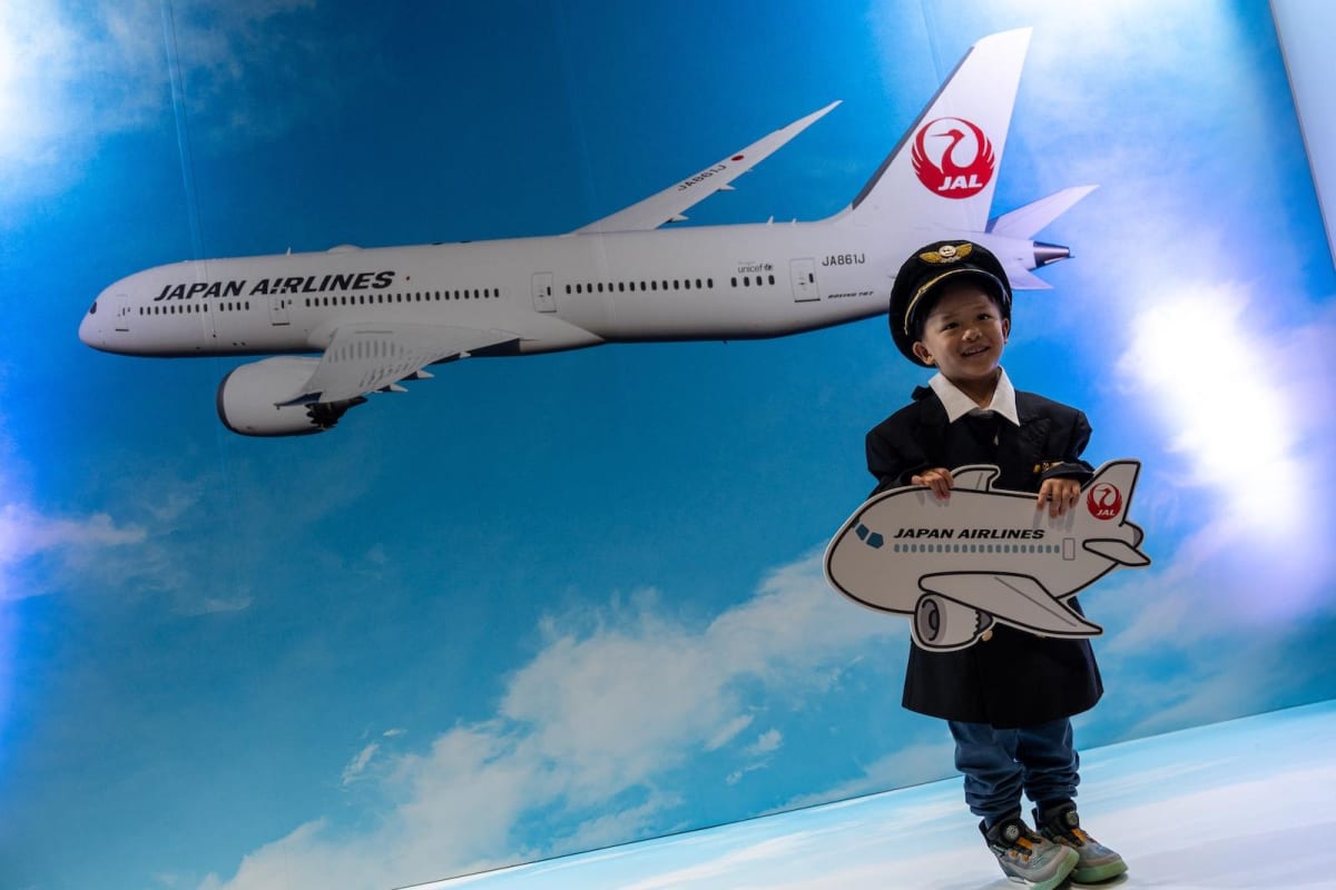 Young boy in pilot uniform poses proudly at Japan Airlines booth during Hong Kong aviation expo