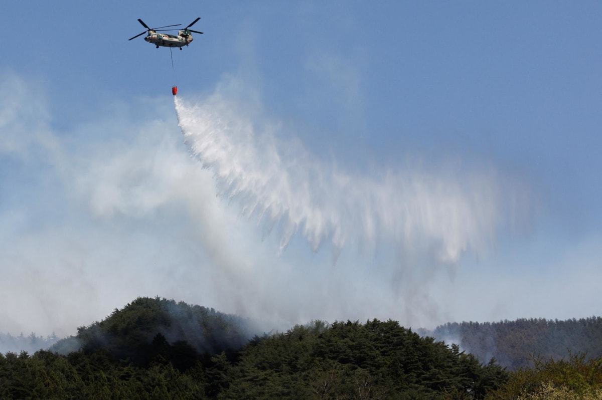 ** Helicopter conducts water-dropping operations over forested mountains during wildfire response in Iwate Prefecture