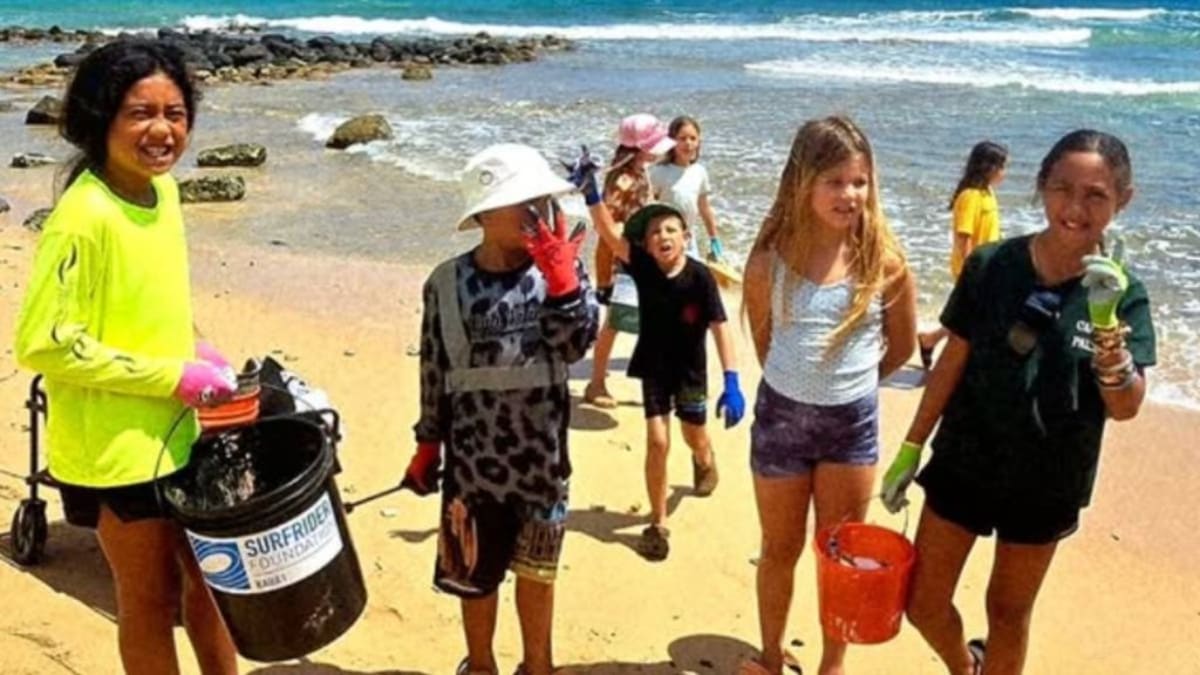 ** Children and adult volunteers pose with trash bags during Surfrider Kauai beach cleanup event