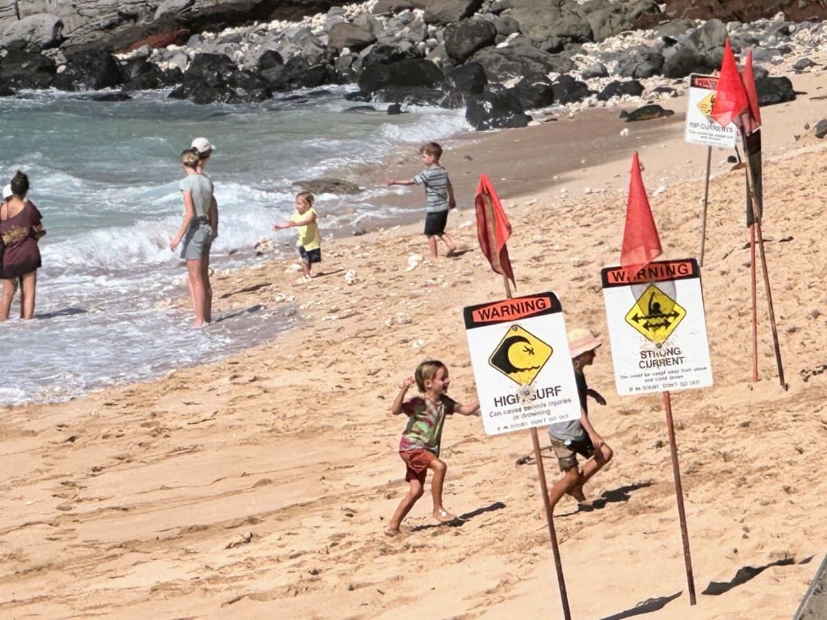 Volunteer safety ambassador speaking with beachgoers at tropical Maui beach with ocean waves behind them
