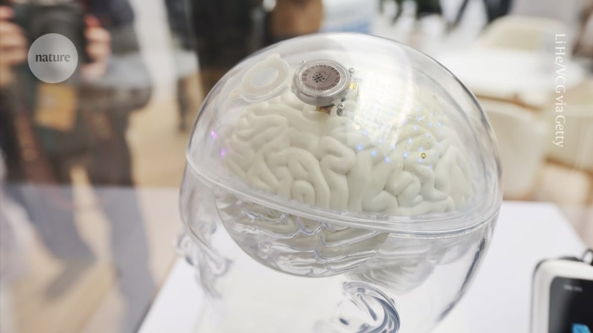Close-up of small circular brain-computer interface device next to human hand for scale