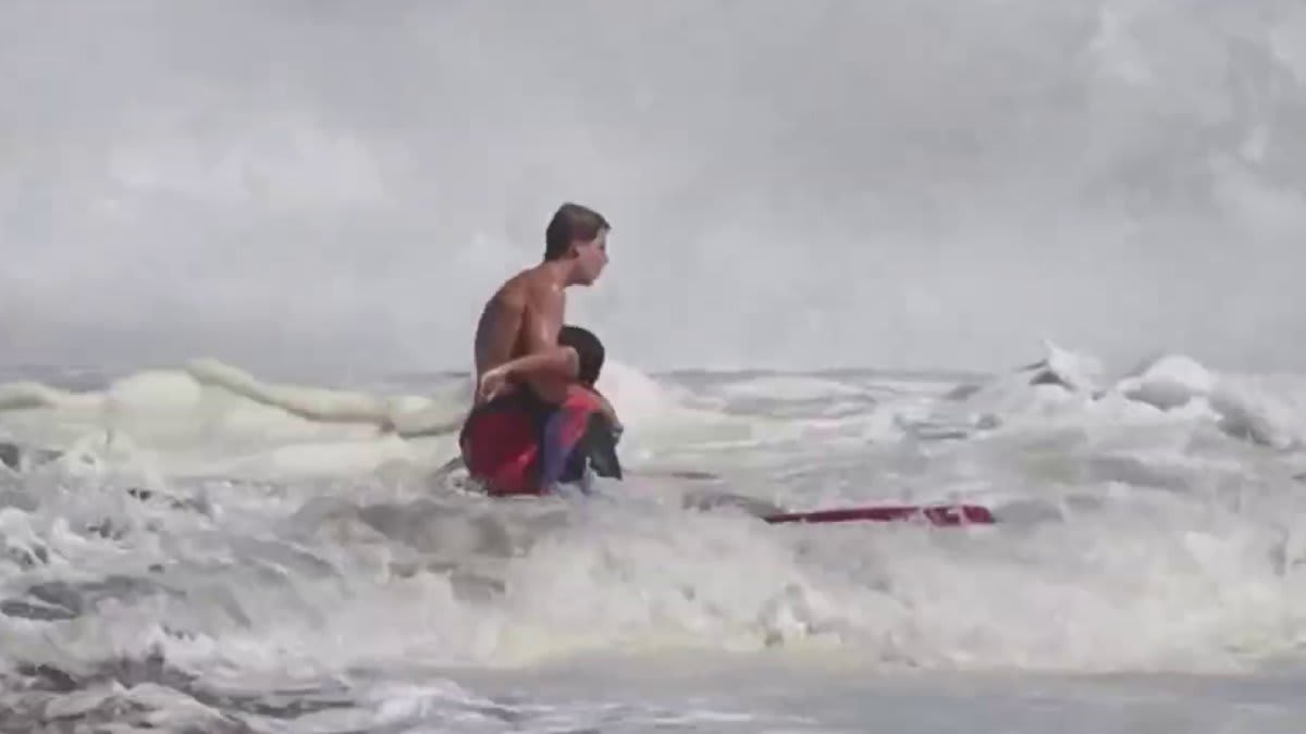 Teen lifeguard rescuing young swimmer in rough ocean waves at Santa Cruz beach
