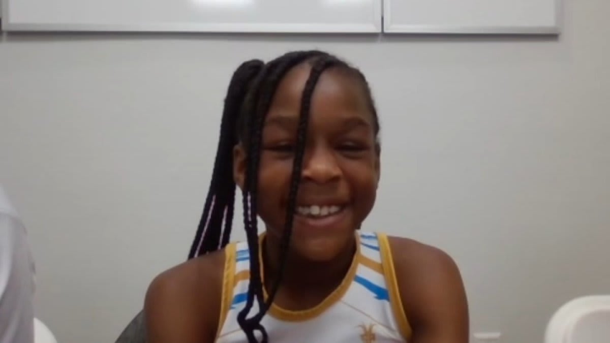 Young girl in racing uniform crossing finish line at outdoor track meet