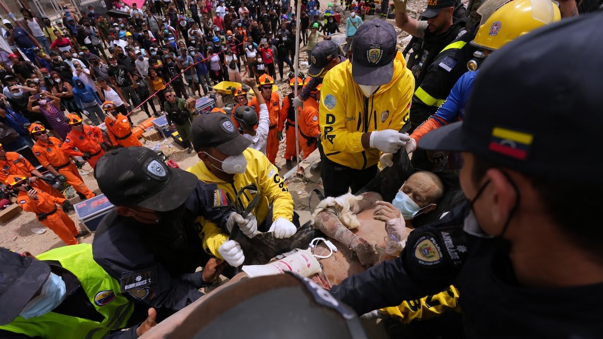 Rescue workers in hard hats carrying earthquake survivor through rubble in Venezuela coastal region