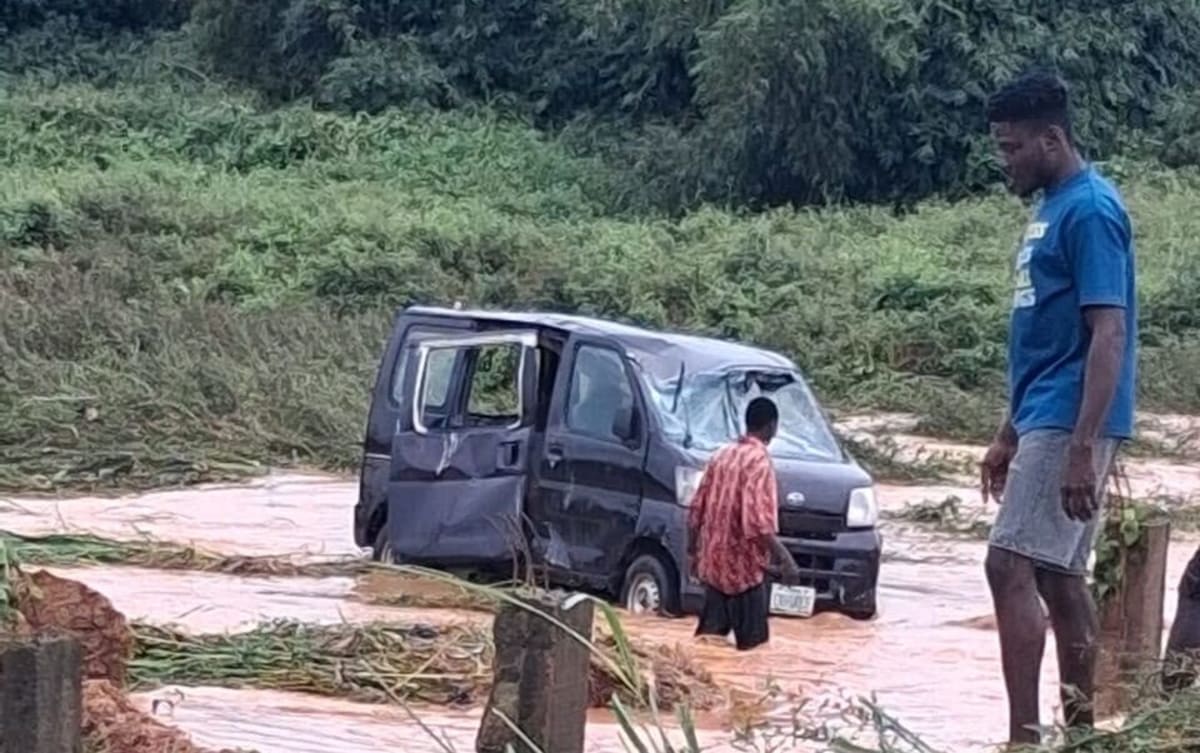 Police officers and community members conducting flood rescue operations on submerged road in Nigeria