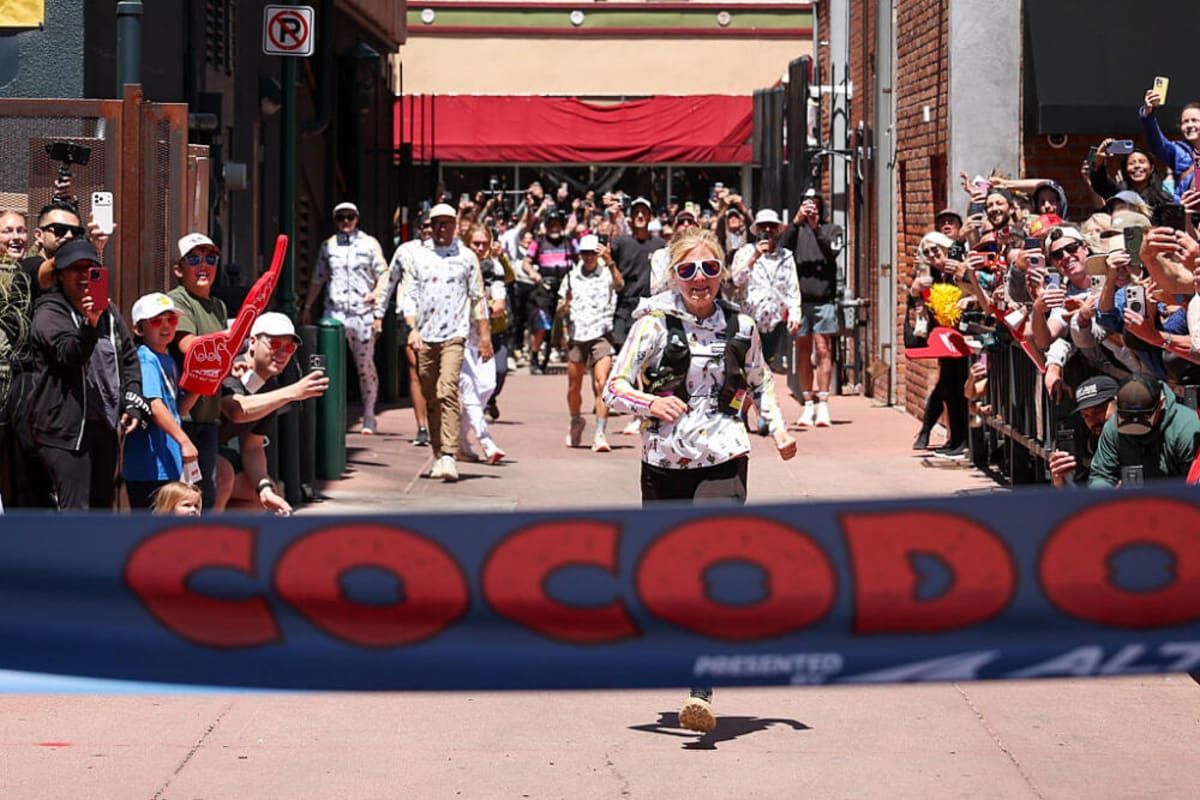** Rachel Entrekin crossing finish line at Cocodona 250 ultramarathon surrounded by cheering crowds