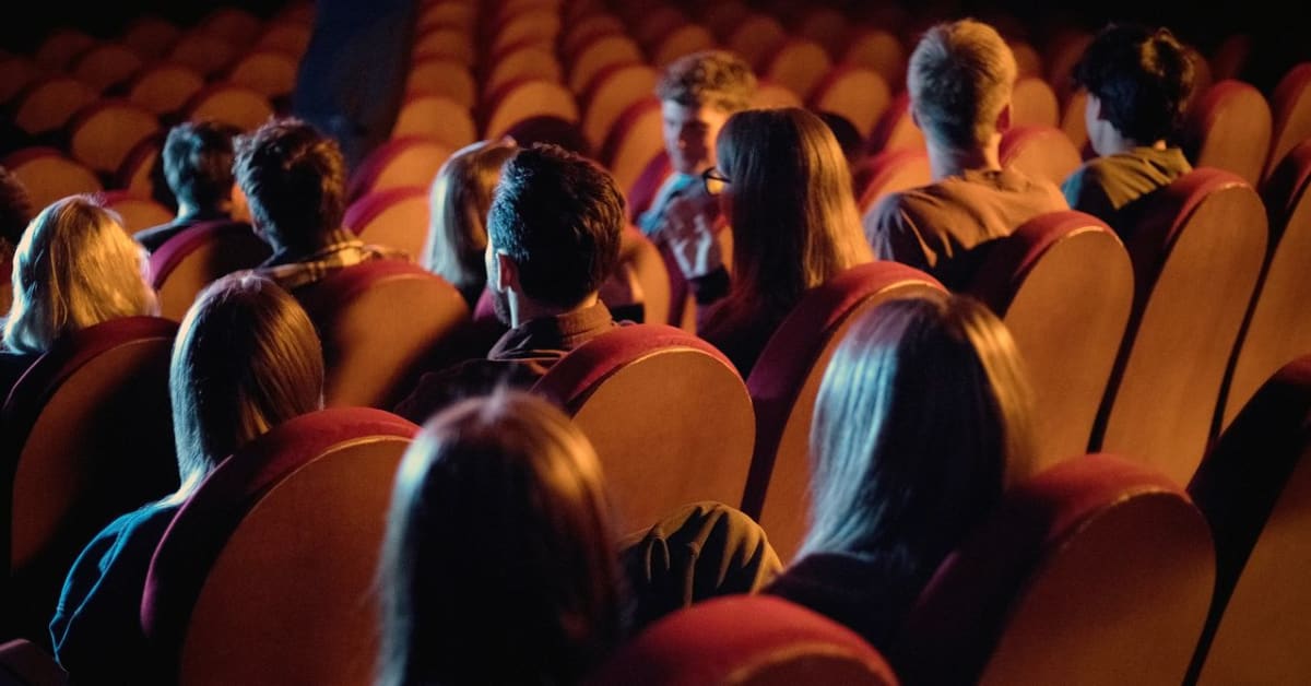 Movie theater audience watching a black and white film on a large screen