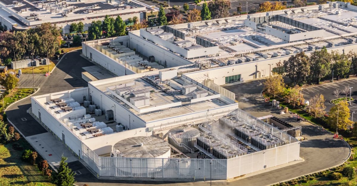 Modern data center cooling towers with water vapor rising against blue sky