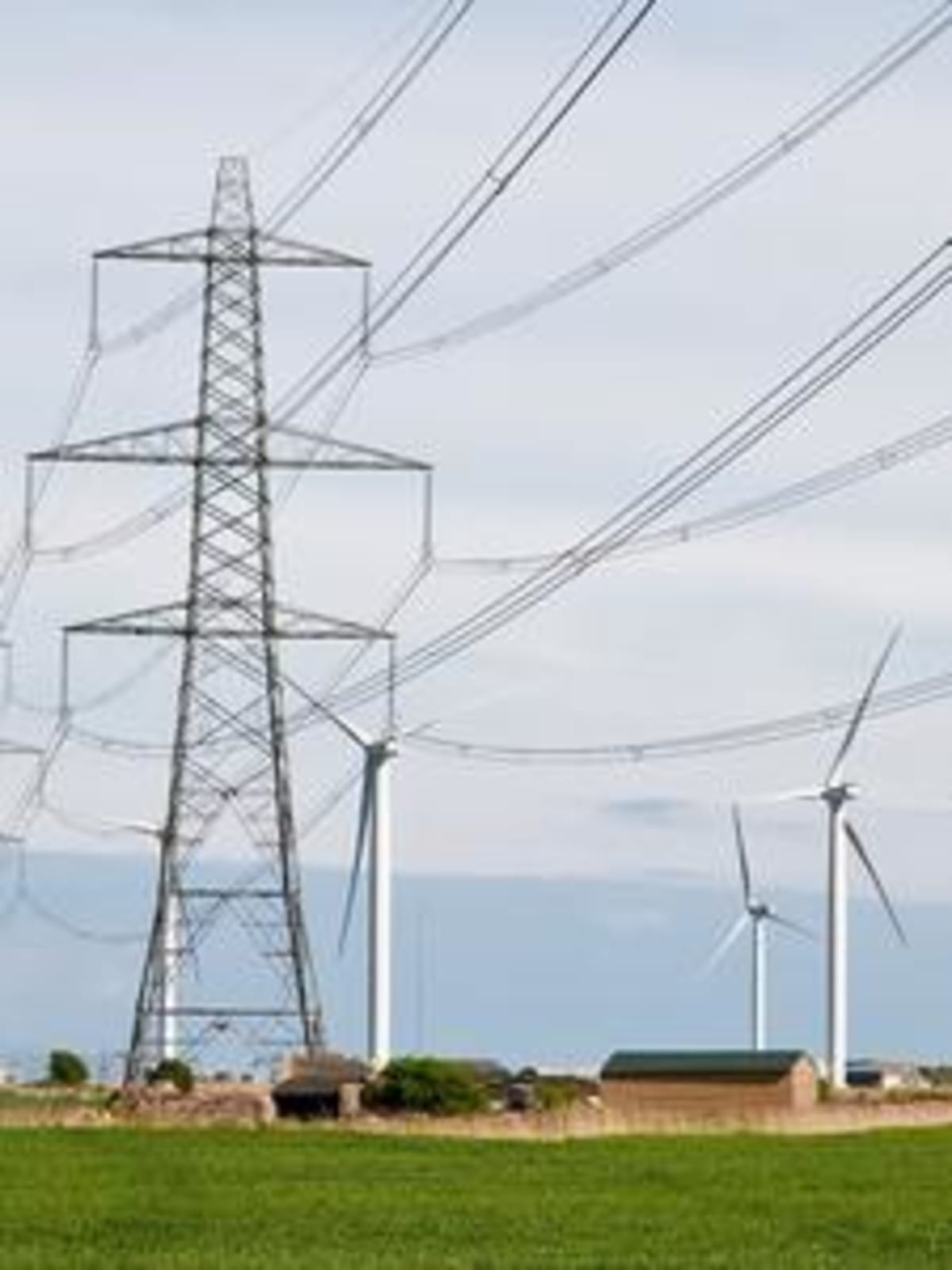 Wind farm turbines standing against sky in East Sussex, England with power transmission lines