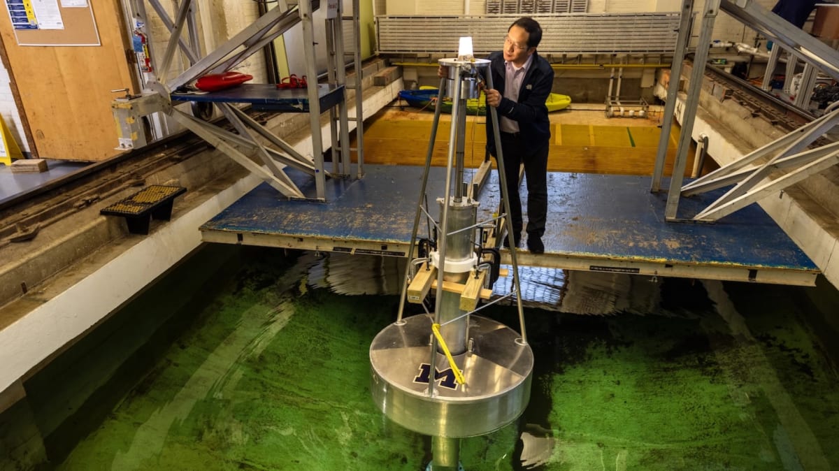 ** University of Michigan professor Lei Zuo standing beside early wave energy converter prototype framed with PVC pipes