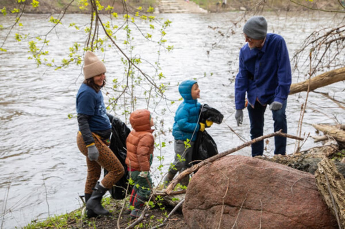 Large diverse group of volunteers wearing gloves collecting trash bags along Milwaukee riverbank
