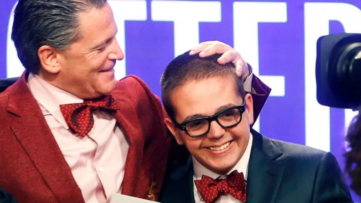 Dan Gilbert standing beside photo of his late son Nick Gilbert who died from neurofibromatosis