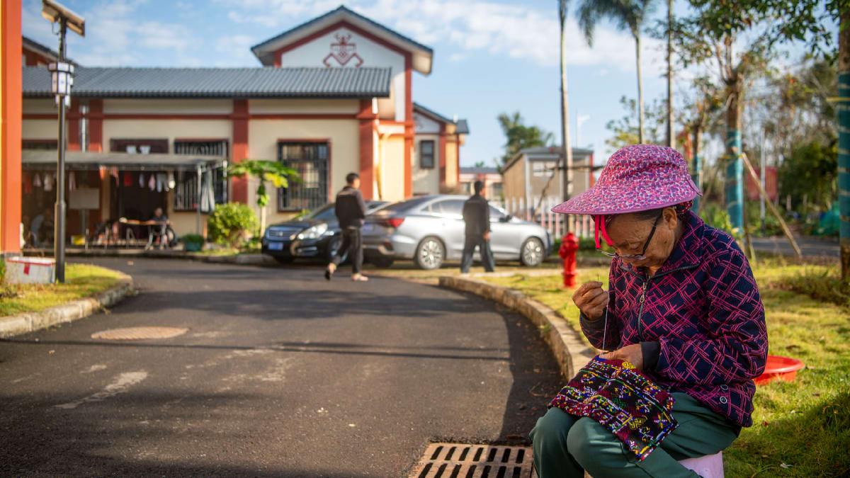 ** Rural villager weaving traditional Miao embroidery at village entrance in Hainan Province, China