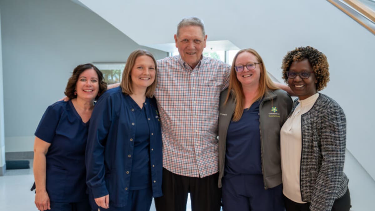Cancer survivor Bill Osborne in green Hulk wig with Graham Cancer Center research team members smiling in hospital lobby