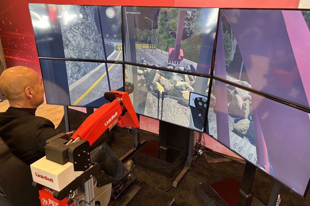 Miniature mechanical excavator arm controller next to immersive virtual training display screens