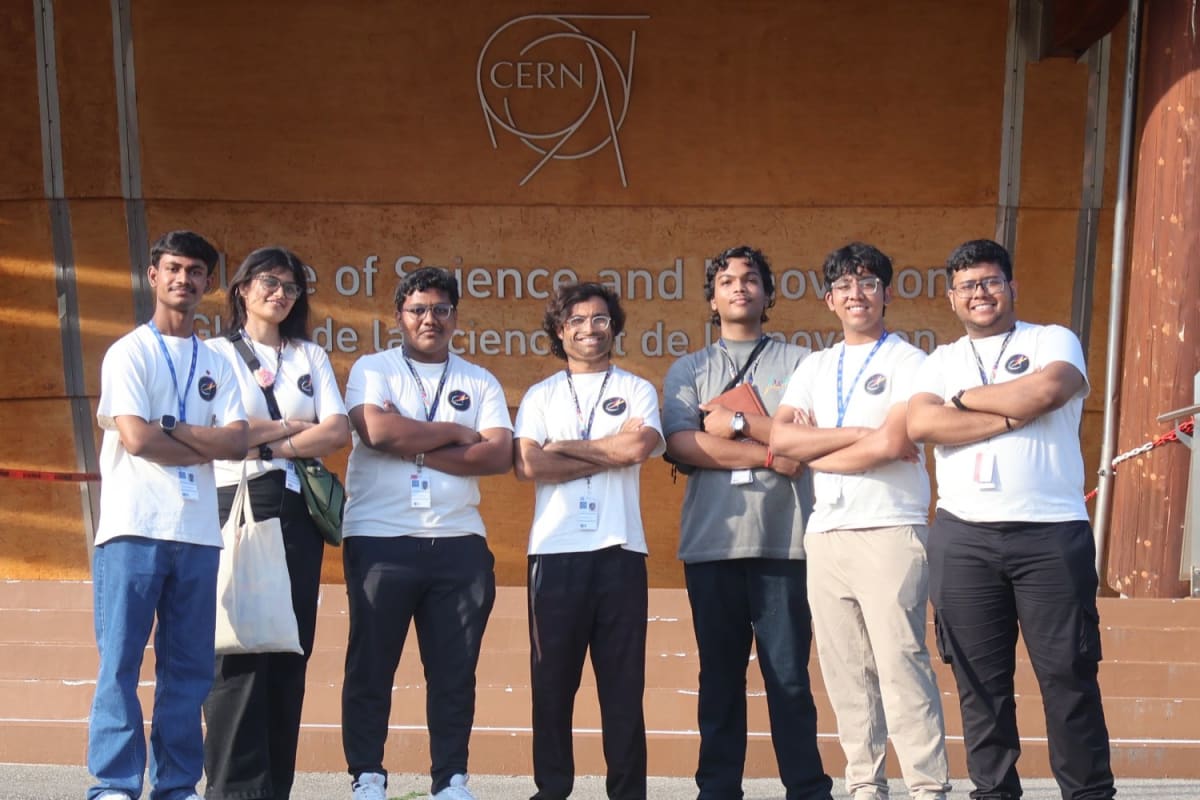 MIT graduate student stands with six Indian high school students at CERN laboratory