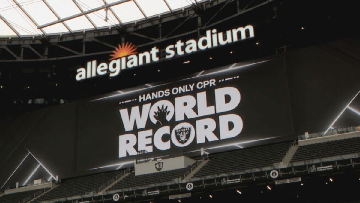 Las Vegas Raiders player Treydan Stukes teaching community members CPR on training mannequins during world record attempt