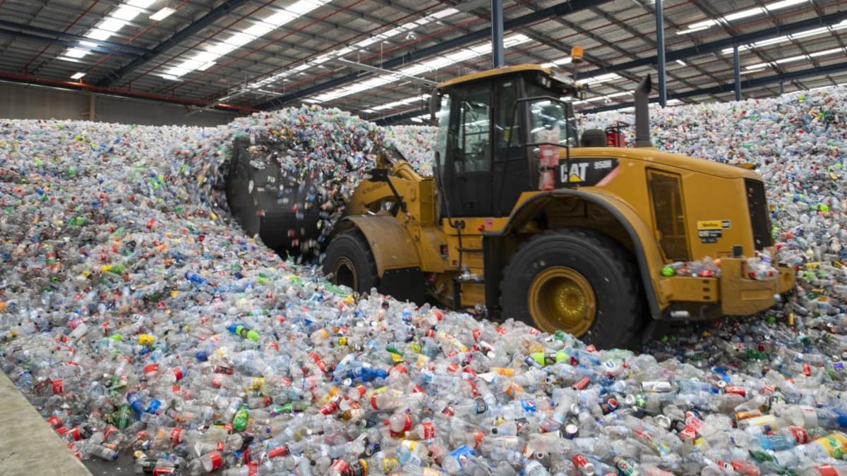 Person depositing empty bottles and cans into Return and Earn recycling machine in New South Wales