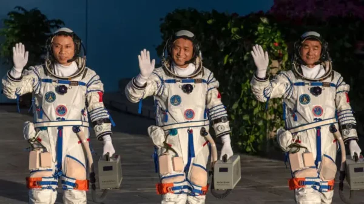 Three astronauts in blue flight suits waving after returning from seven-month space mission