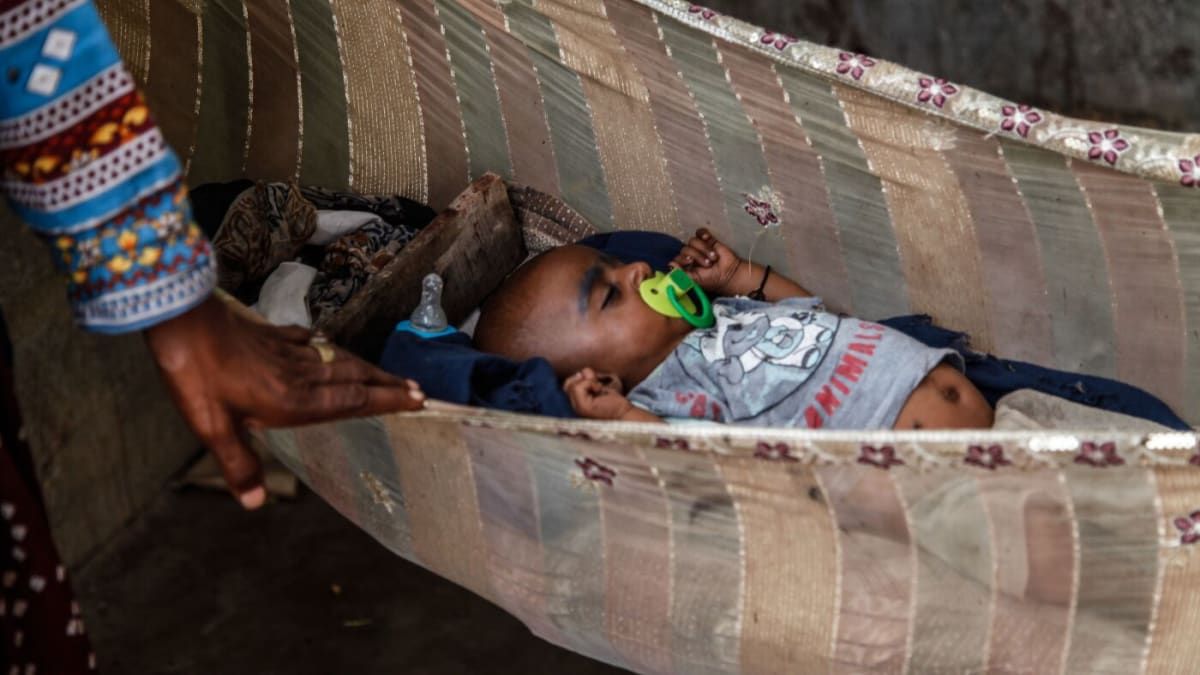 Grandmother gently rocks baby's hammock in Rehri Goth, Pakistan community setting