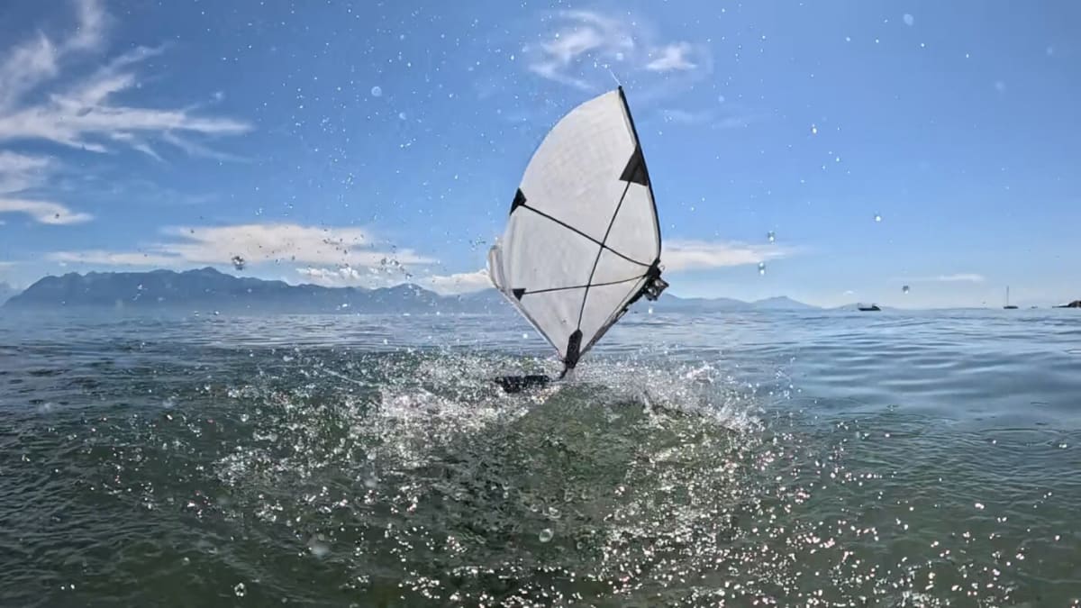 Small white aerial-aquatic robot with translucent wings lifting off from calm lake water