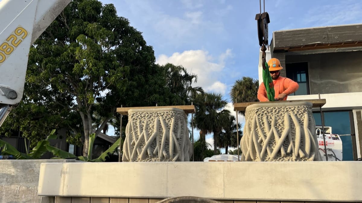 Workers on floating barge install textured mangrove planter onto smooth concrete seawall in Florida canal