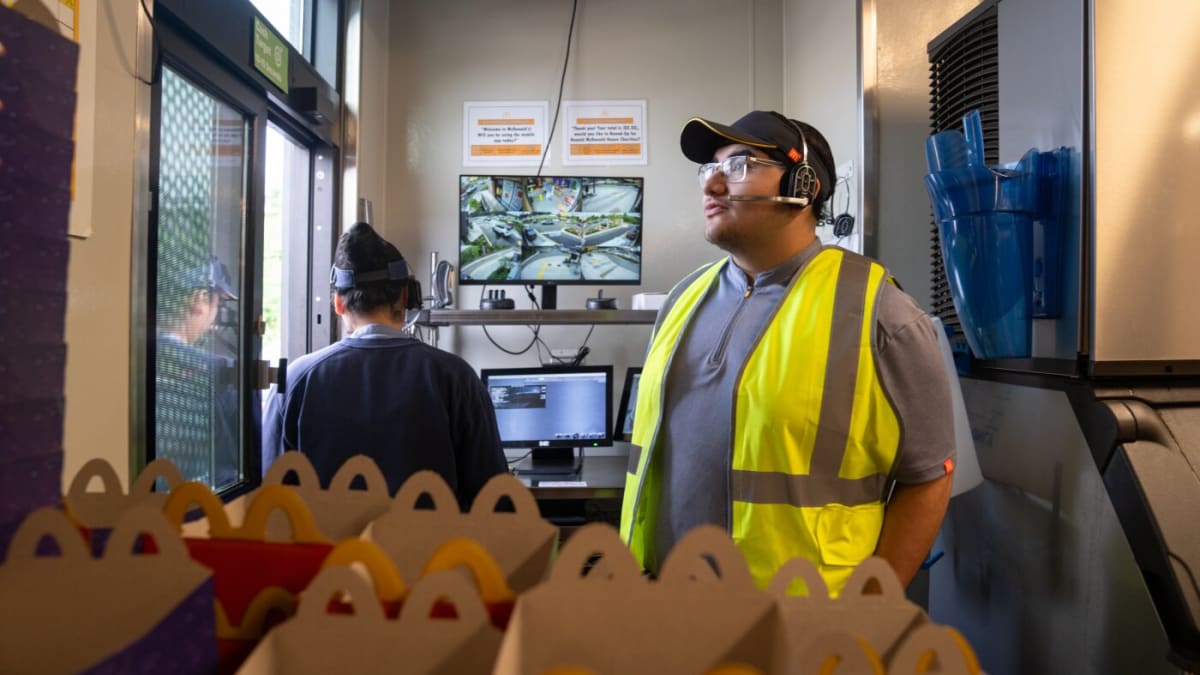 Young McDonald's employee taking drive-through orders while smiling at customer in Maryland restaurant