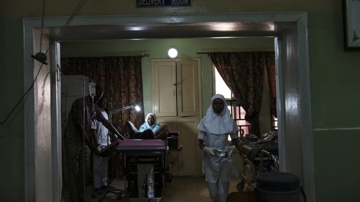 Senior midwife providing postpartum care to new mother in Nigerian healthcare facility