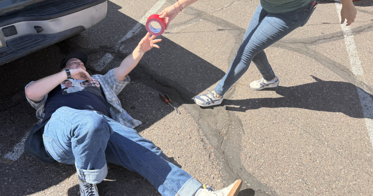 ** Volunteers lean over open car trunk replacing broken tail light bulb in Phoenix parking lot