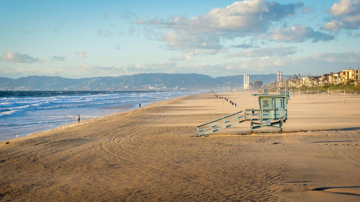 Volunteers cleaning a sunny California beach with buckets and gloves during community ocean conservation event