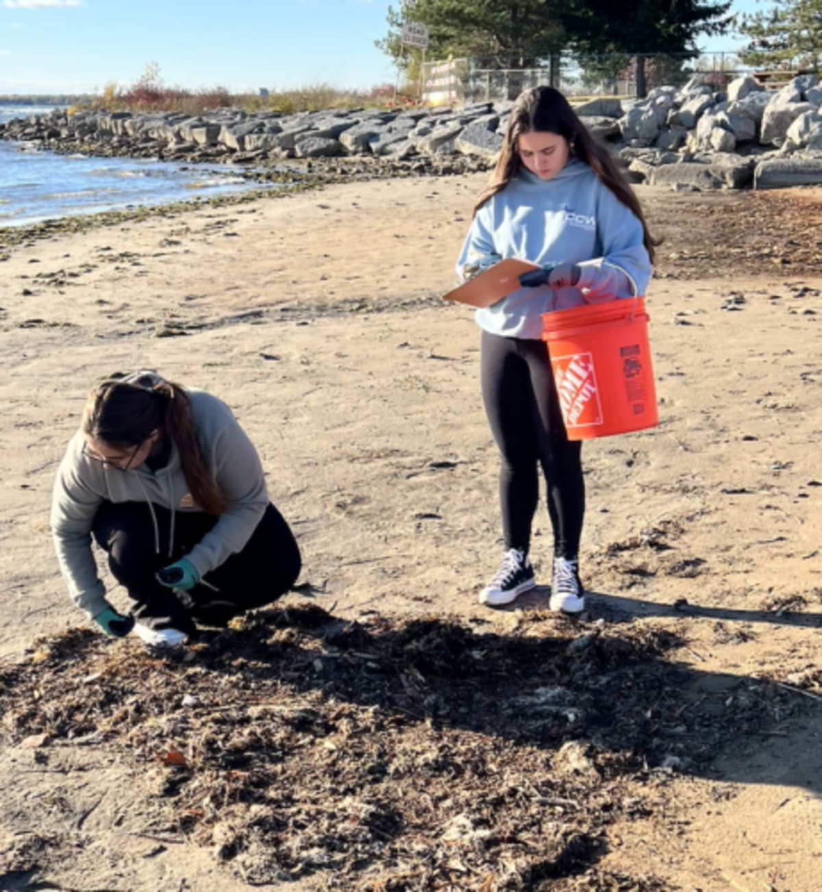 Two high school students collecting trash on Starlite Beach along Lake Huron shoreline