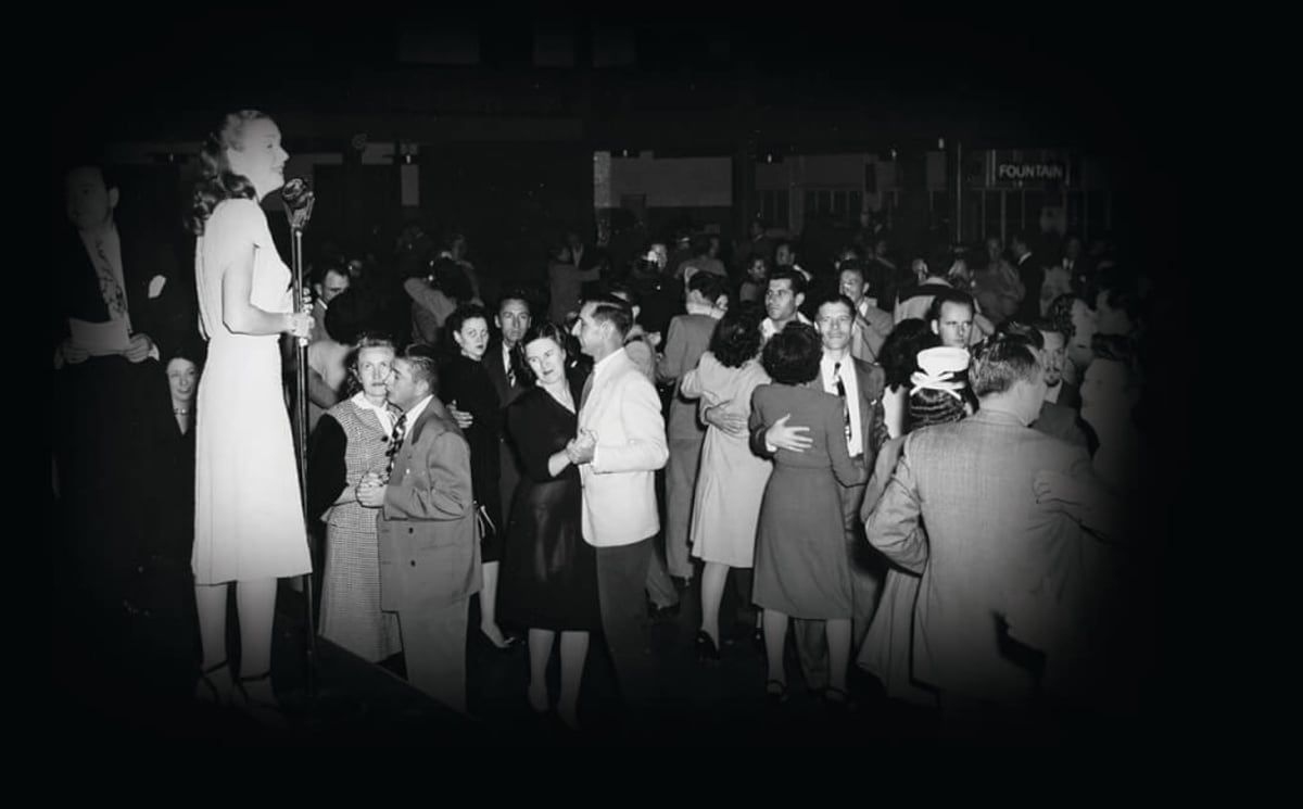 Large crowd of people swing dancing together on grass near historic Balboa Pier in Newport Beach